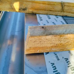 constructionmonter@gmail.com - Fragment konstrukcji dachu z widocznymi elementami drewnianymi, srebrną blachą i membraną dachową z nadrukiem Wigluv, uchwycony z bliskiej perspektywy.