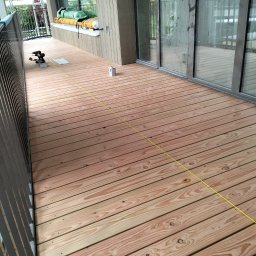 constructionmonter@gmail.com - Nowo ułożony drewniany taras z widocznymi śladami po wkrętach, narzędzia i akcesoria do montażu, żółta linia wyznaczająca kierunek, widok z boku balkonu.