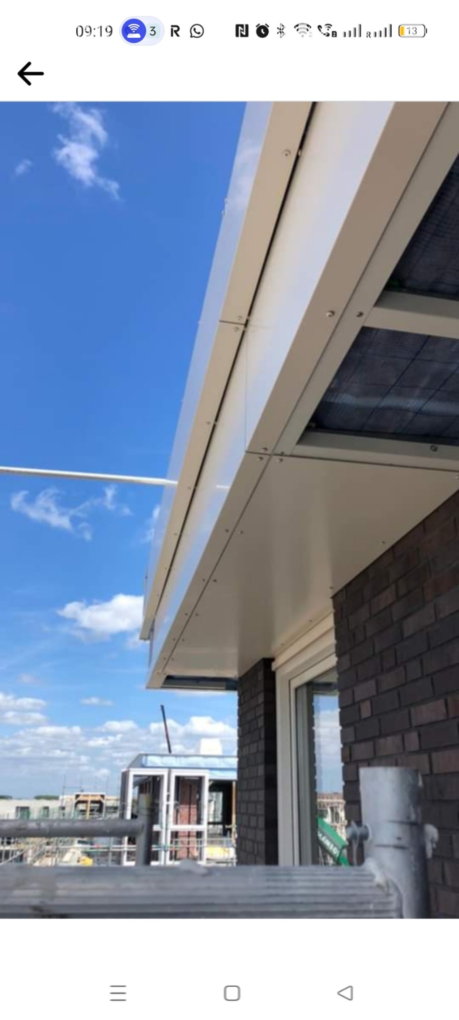 Montaż podbitki dachowej z paneli PCV, widok z rusztowania na tle błękitnego nieba.