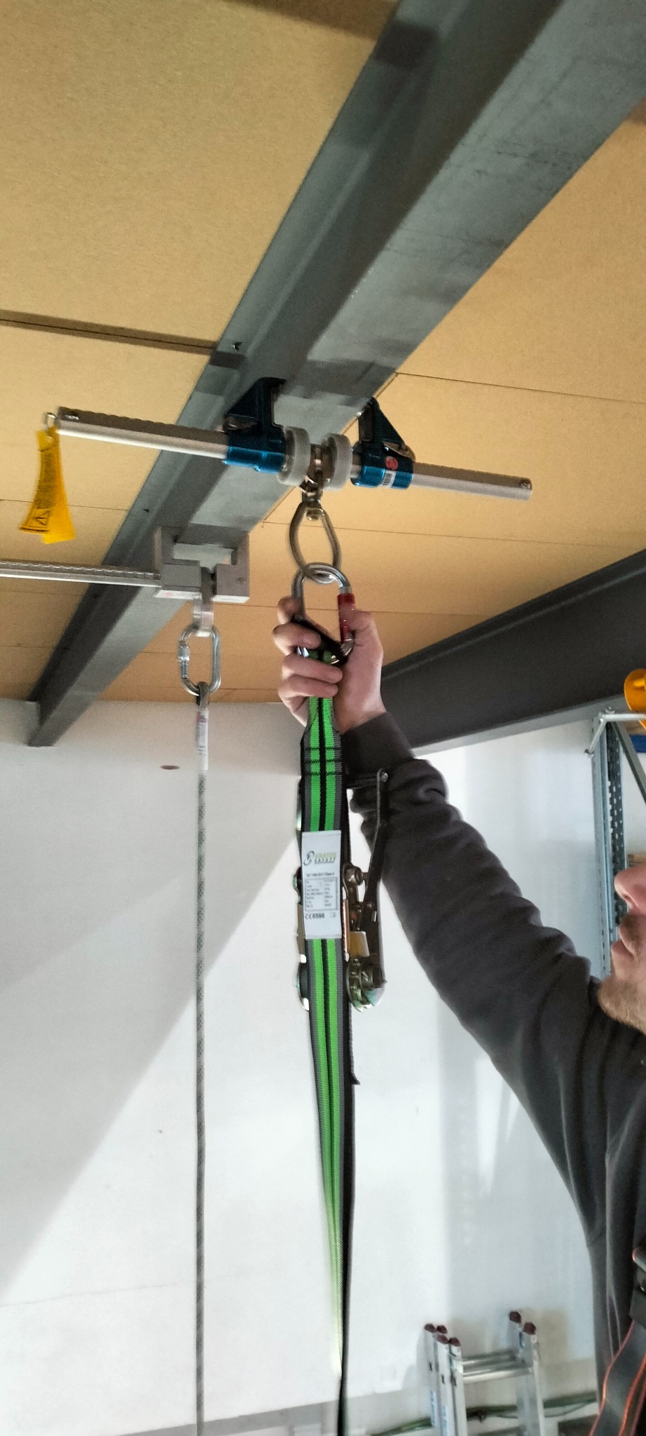 Mężczyzna trzyma uprząż zabezpieczającą przymocowaną do stalowej belki z zamocowanym systemem kotwiczenia nad głową.