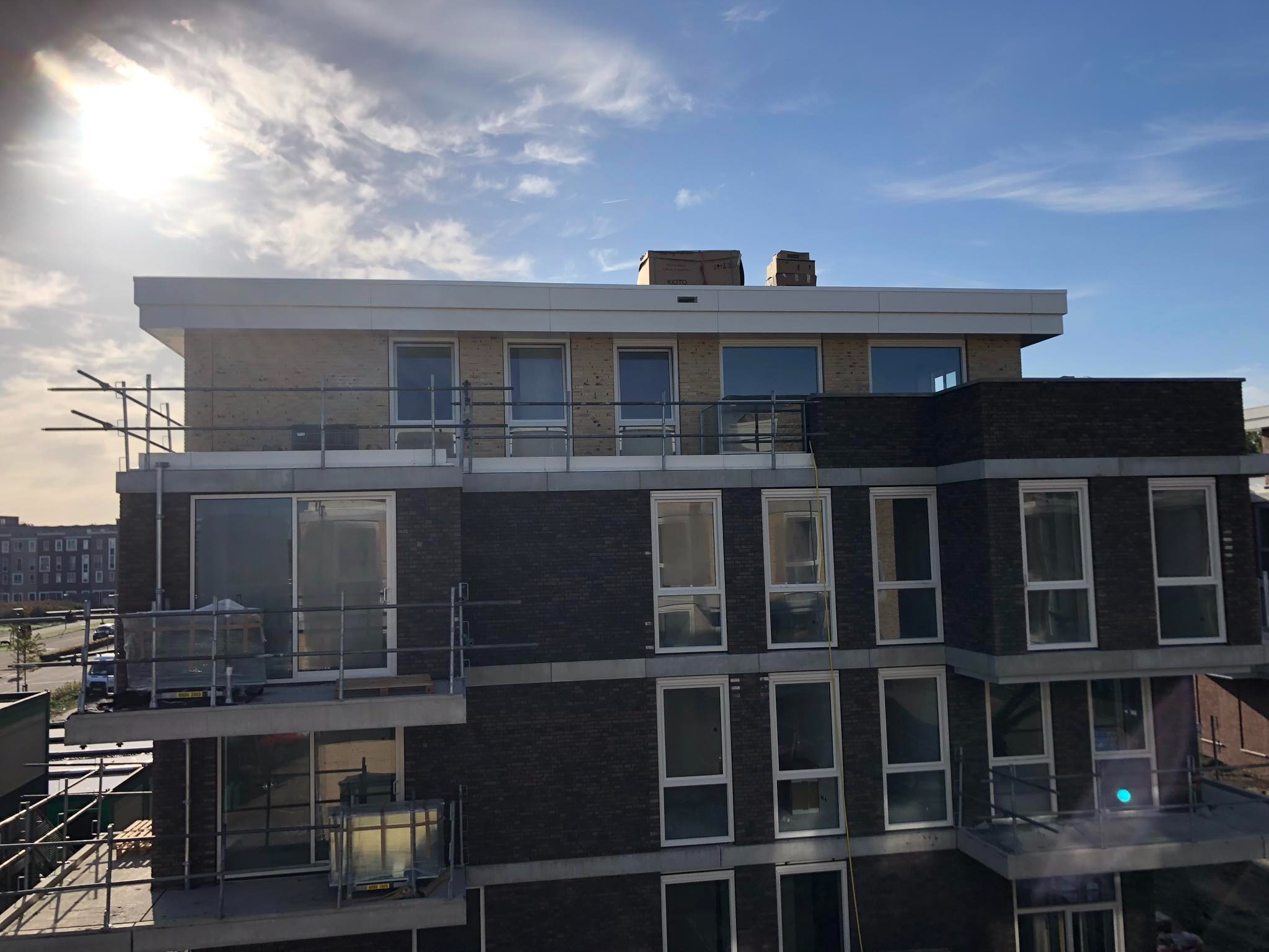 Wielopiętrowy budynek mieszkalny z balkonami w trakcie budowy, widoczne rusztowania i materiały budowlane na balkonach, słoneczny dzień.