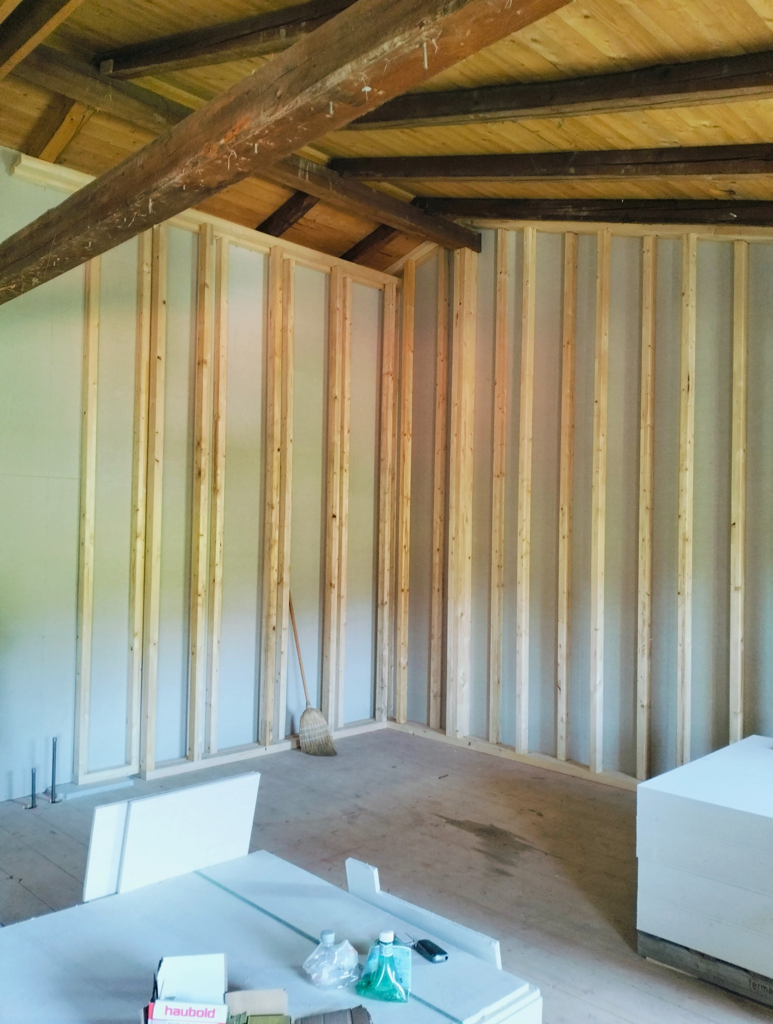 Wnętrze w trakcie remontu: drewniana konstrukcja szkieletowa ścian działowych z widocznymi belkami stropowymi, płyty gipsowe, narzędzia i materiały budowlane na podłodze.