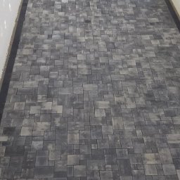 Wolfheart prace brukarskie - Ukończona ścieżka z szarej kostki brukowej ułożonej we wzór, widok z góry. W tle pracownicy i sprzęt budowlany.