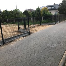 Mariusz Głąb - Nowoczesne ogrodzenie panelowe z betonową podmurówką i bramą wjazdową, widoczne z perspektywy chodnika. Dom i zieleń w tle.