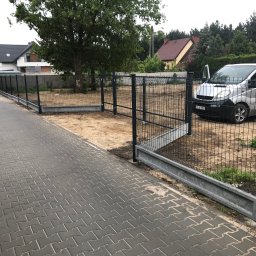 Mariusz Głąb - Nowoczesne, czarne ogrodzenie panelowe z podmurówką betonową, widok z zewnątrz posesji, szara kostka brukowa, srebrny van z otwartymi drzwiami w tle.