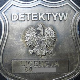 Black Falcon Group SŁAWOMIR WIŚNIOWSKI - Metalowa odznaka detektywa z orłem w koronie i napisem 'Licencja' z zamazanym numerem, na czarnym tle. Odznaka w kształcie tarczy.