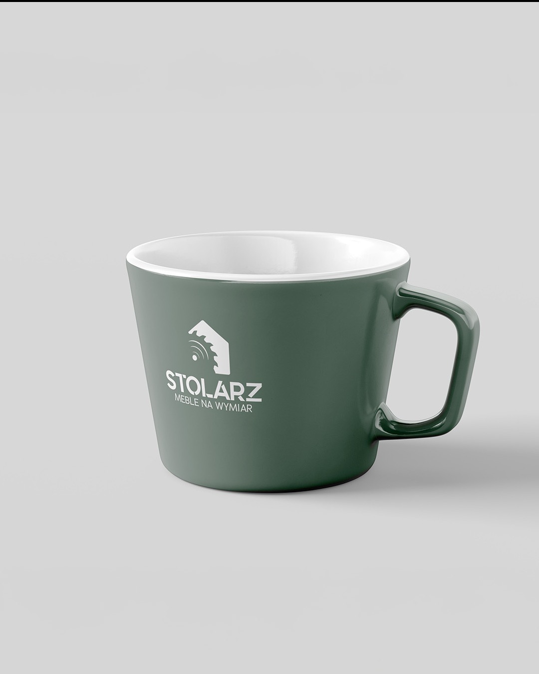 Zielony kubek z białym wnętrzem prezentujący logo firmy stolarskiej na szarym tle.