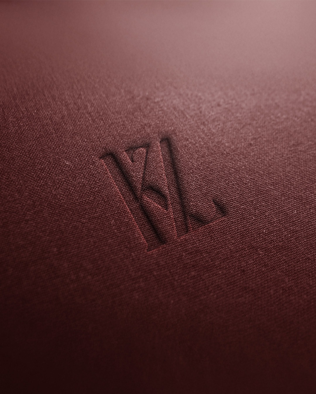 Wytłoczone logo 'KZ' na bordowej, teksturowanej powierzchni, imitującej tkaninę.