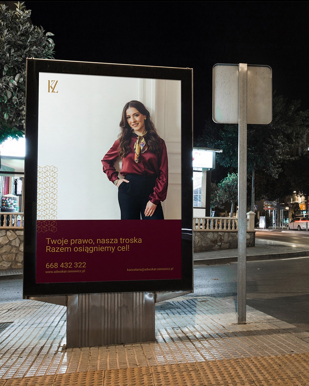 Billboard reklamowy na ulicy nocą, prezentujący wizerunek uśmiechniętej kobiety w eleganckiej bluzce i informacje kontaktowe do kancelarii adwokackiej.
