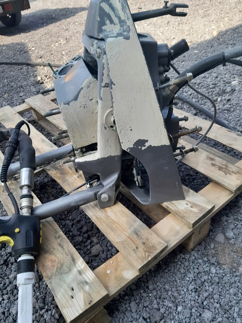 Zdemontowany, brudny silnik łodzi na drewnianej palecie, widoczne ślady piasku i osadów, przygotowany do czyszczenia przemysłowego.