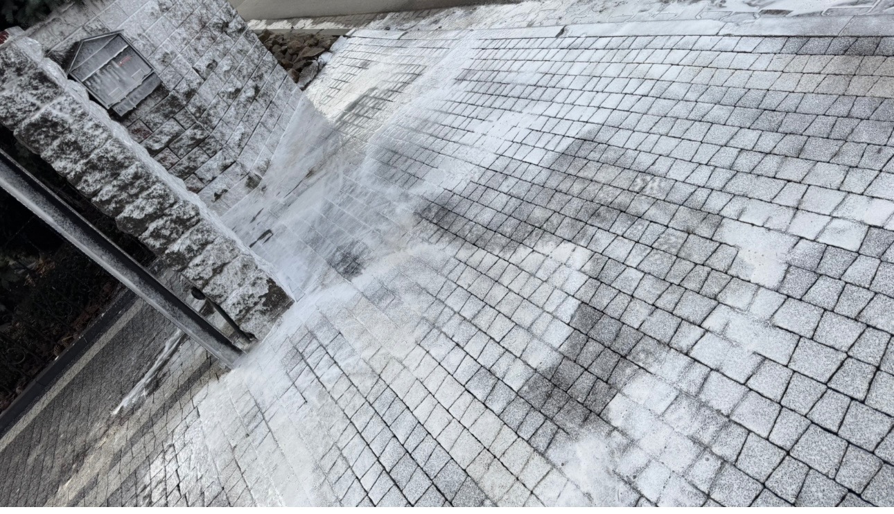 Częściowo oczyszczona z zabrudzeń kostka brukowa, widoczne ślady mycia pod ciśnieniem, zarys budynku w tle.