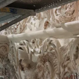 Fragment odrestaurowanego, ozdobnego gzymsu z motywami roślinnymi i zwierzęcymi, widoczny spod metalowego rusztowania.