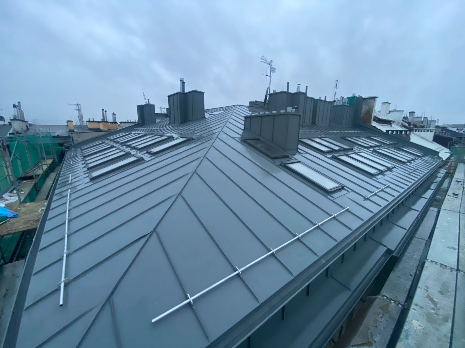 Szary dach z blachy trapezowej z oknami dachowymi i odgromem na tle pochmurnego nieba, widok z góry.