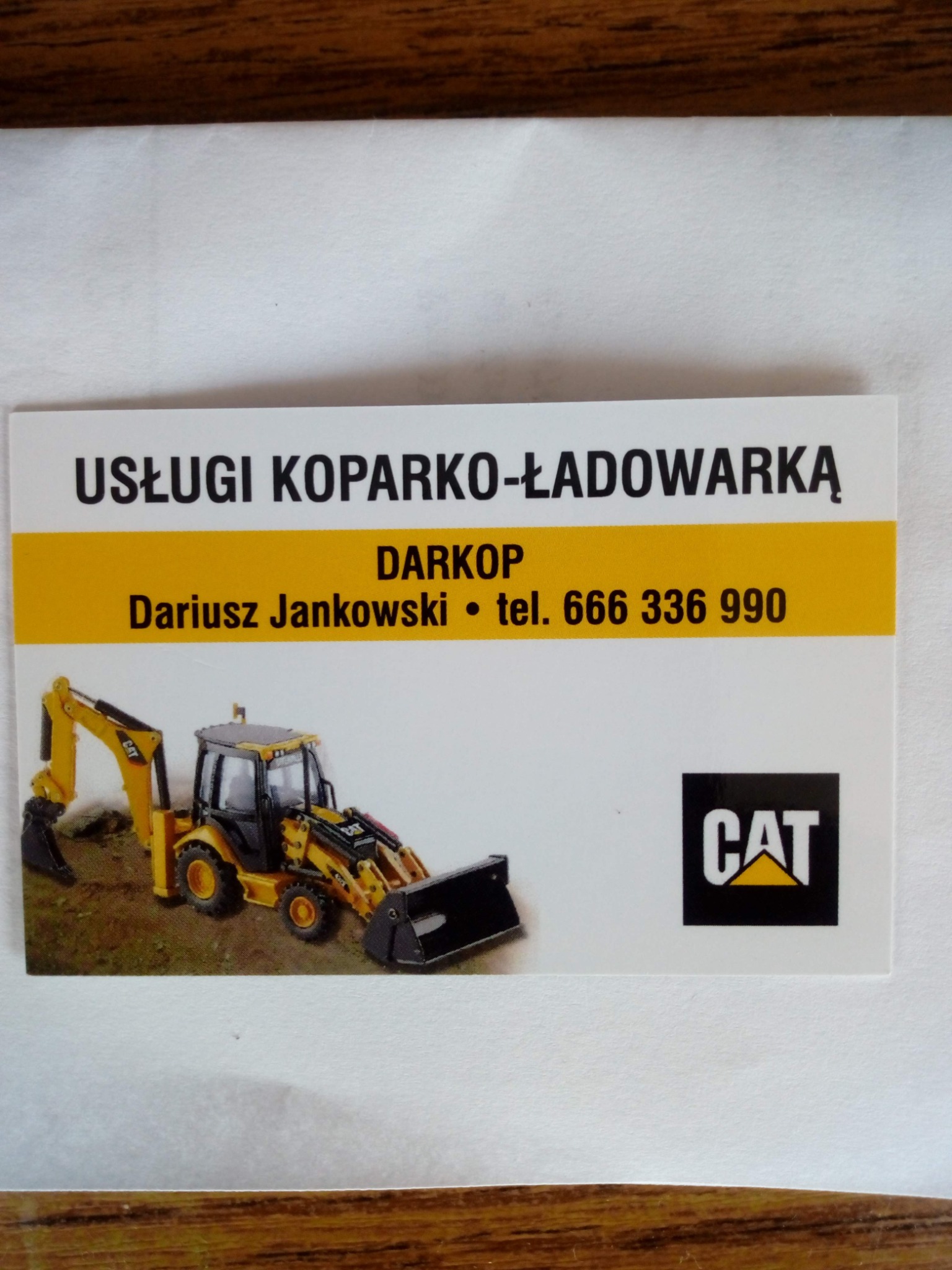Wizytówka firmy DARKOP z Lisówek oferującej usługi koparko-ładowarką, z ilustracją żółtej maszyny CAT.