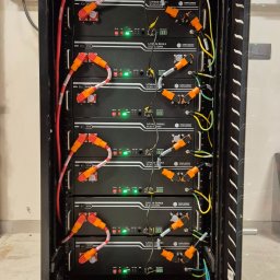 DKKD.PL - Rząd akumulatorów litowo-jonowych w czarnej szafie rack, z okablowaniem i diodami LED, widoczne etykiety 'Lithium Series 51.2V'.