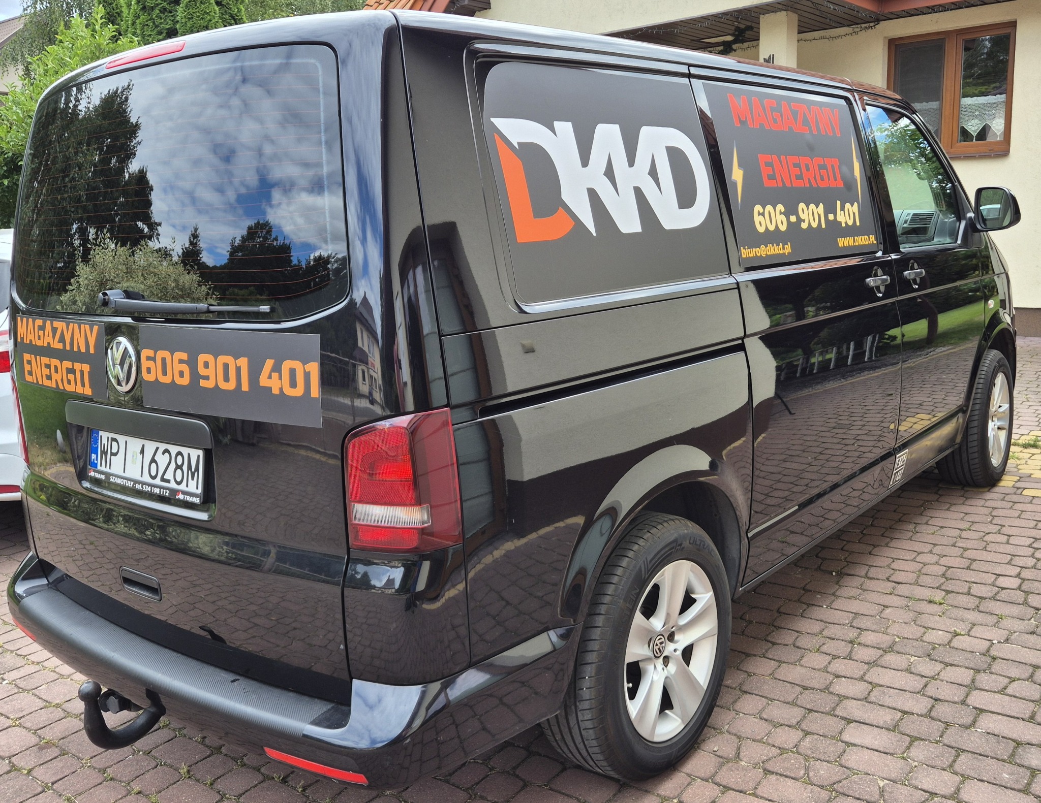 Czarny samochód dostawczy firmy z Dobrzenicy, oklejony logo i informacjami o magazynach energii oraz numerem telefonu kontaktowego.