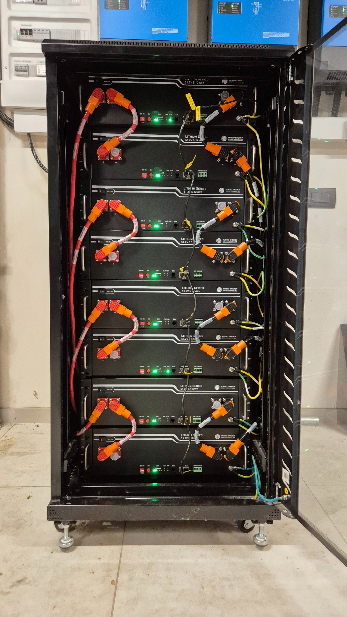 Rząd akumulatorów litowo-jonowych w czarnej szafie rack, z okablowaniem i diodami LED, widoczne etykiety 'Lithium Series 51.2V'.