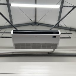 TEL-CARS Andrzej Pudło - Biała jednostka klimatyzacyjna zamontowana pod sufitem hali produkcyjnej, widoczne stalowe profile konstrukcyjne i oświetlenie LED.