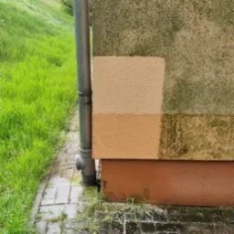 Fragment elewacji przed i po czyszczeniu, widoczne r&oacute;żnice w kolorze i usunięcie zabrudzeń, obok rynna spustowa i trawnik.