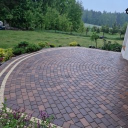 Sebo Dach I Bruk jak nowy - Ułożona kostka brukowa w kształcie wachlarza, obrzeża z jasnego kamienia, trawnik i zieleń w tle. Widok na posesję z bliska, w pochmurny dzień.