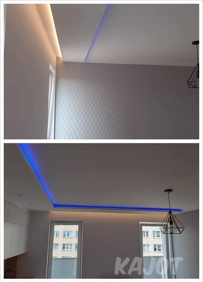 Dwupoziomowy sufit podwieszany z oświetleniem LED: górna część z ciepłym białym światłem, dolna z niebieskim, widoczna lampa wisząca i fragment tapety w geometryczny wzór.