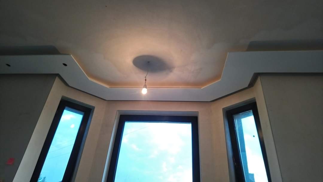 Wykończony sufit z gładzią, ozdobnymi listwami i centralnym oświetleniem w pomieszczeniu z oknami.