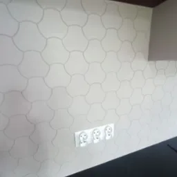 Ściana w kuchni wykończona dekoracyjną gładzią o wzorze zaokrąglonych elementów, z zamontowanymi trzema gniazdkami elektrycznymi, widoczny fragment blatu.