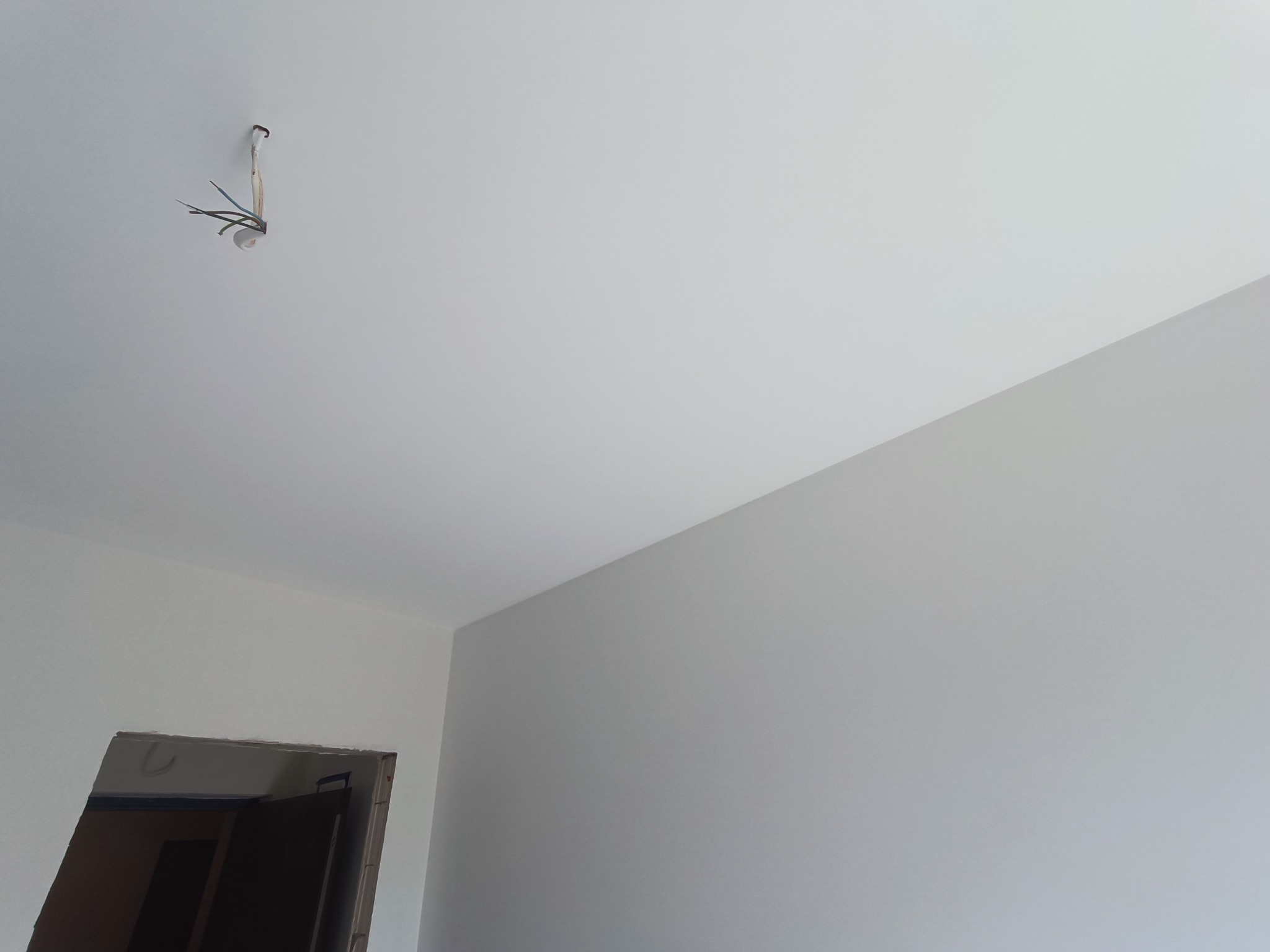 Świeżo pomalowane wnętrze z wystającymi przewodami elektrycznymi z sufitu, widoczne ościeże drzwi