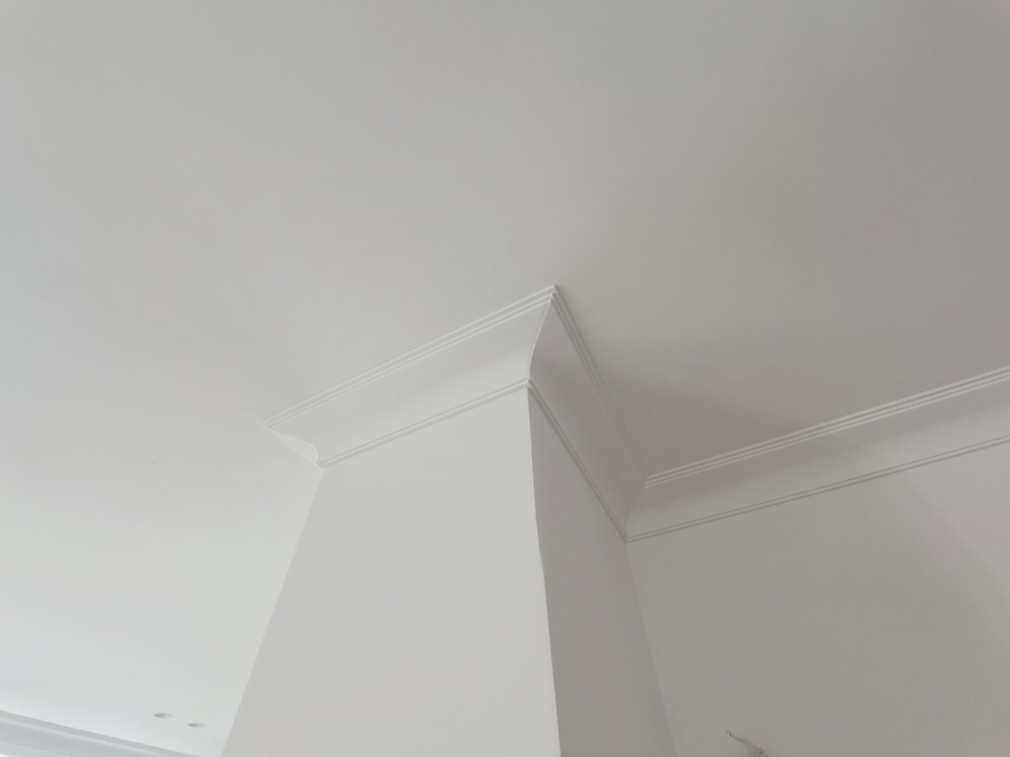 Białe, świeżo pomalowane narożne połączenie ściany i sufitu z dekoracyjnym gzymsem, widoczne z dołu pod kątem.