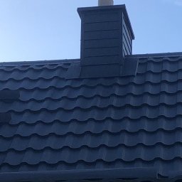 Piotr Kluka - Ciemna blachodachówka z kominem w kolorze, widoczna rynna, błękitne niebo w tle.