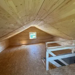 Drewniane poddasze z małym oknem i drewnianą barierką. Widoczne deski na ścianach, suficie i podłodze. Ujęcie z dołu, podkreślające przestrzeń i strukturę drewna.