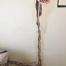 Remonty.GZ - Ściana z wyciętym bruzdą pod kable elektryczne, widoczne pomarańczowe puszki instalacyjne i białe przewody.