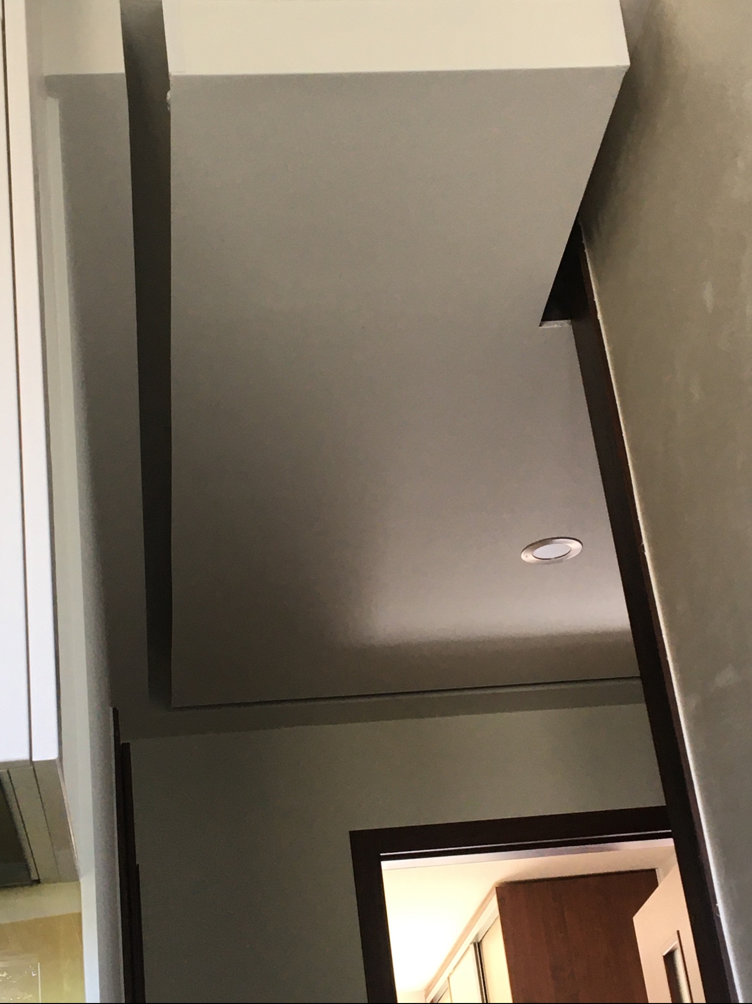 Fragment wnętrza z widocznym sufitem podwieszanym, oświetleniem punktowym i fragmentem ramy drzwiowej z ciemnego drewna.