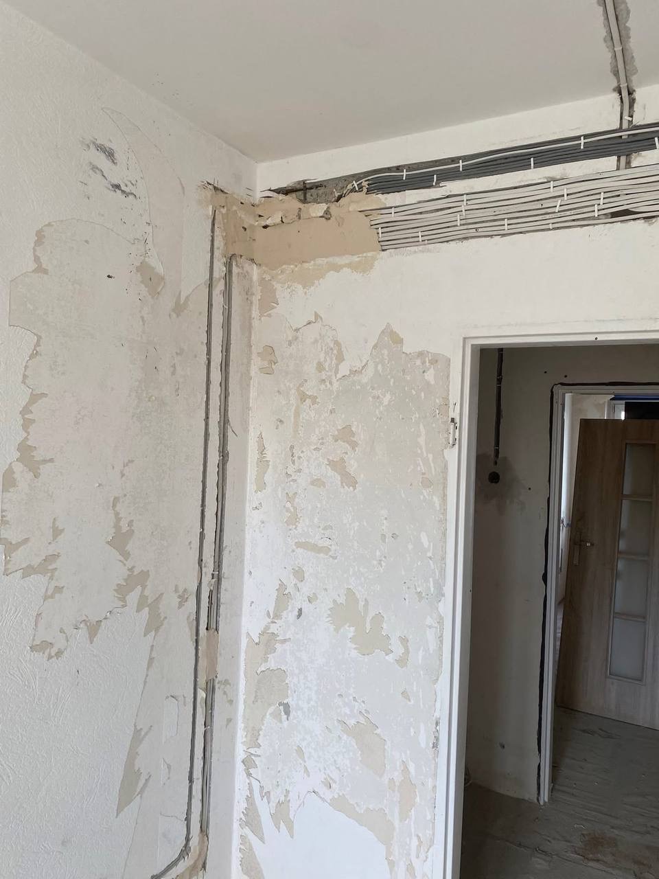 Ściana w trakcie remontu z widocznymi przewodami elektrycznymi pod sufitem i pionowymi rurkami w ścianie, przygotowana do dalszych prac wykończeniowych.