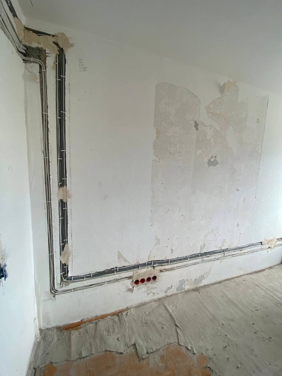 Ściana w trakcie remontu z widocznymi przewodami elektrycznymi ułożonymi wzdłuż ścian, przygotowanymi do dalszych prac wykończeniowych.