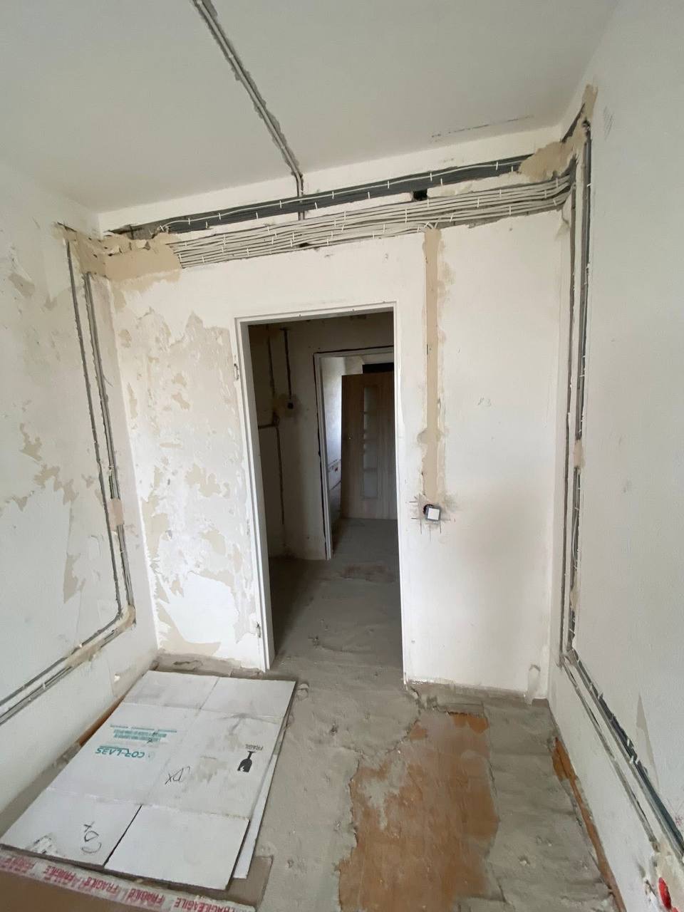 Wnętrze w trakcie remontu z widocznymi przewodami elektrycznymi na ścianach i suficie, przygotowane do tynkowania. Na podłodze leżą kartony zabezpieczające.