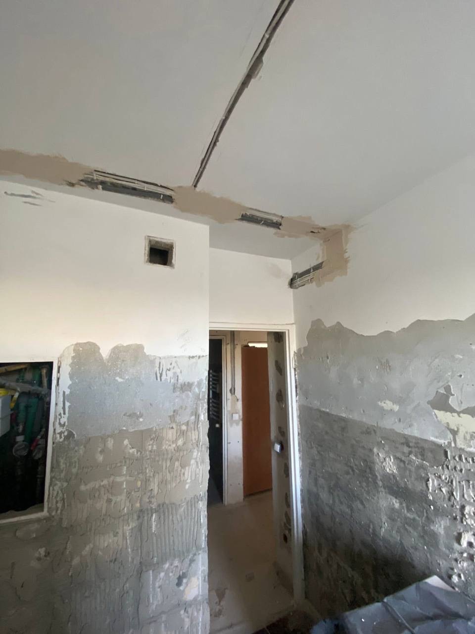 Wnętrze w trakcie remontu: ściany z resztkami tynku, widoczne kable elektryczne pod sufitem, przygotowane do montażu oświetlenia. Prace instalacyjne w toku.