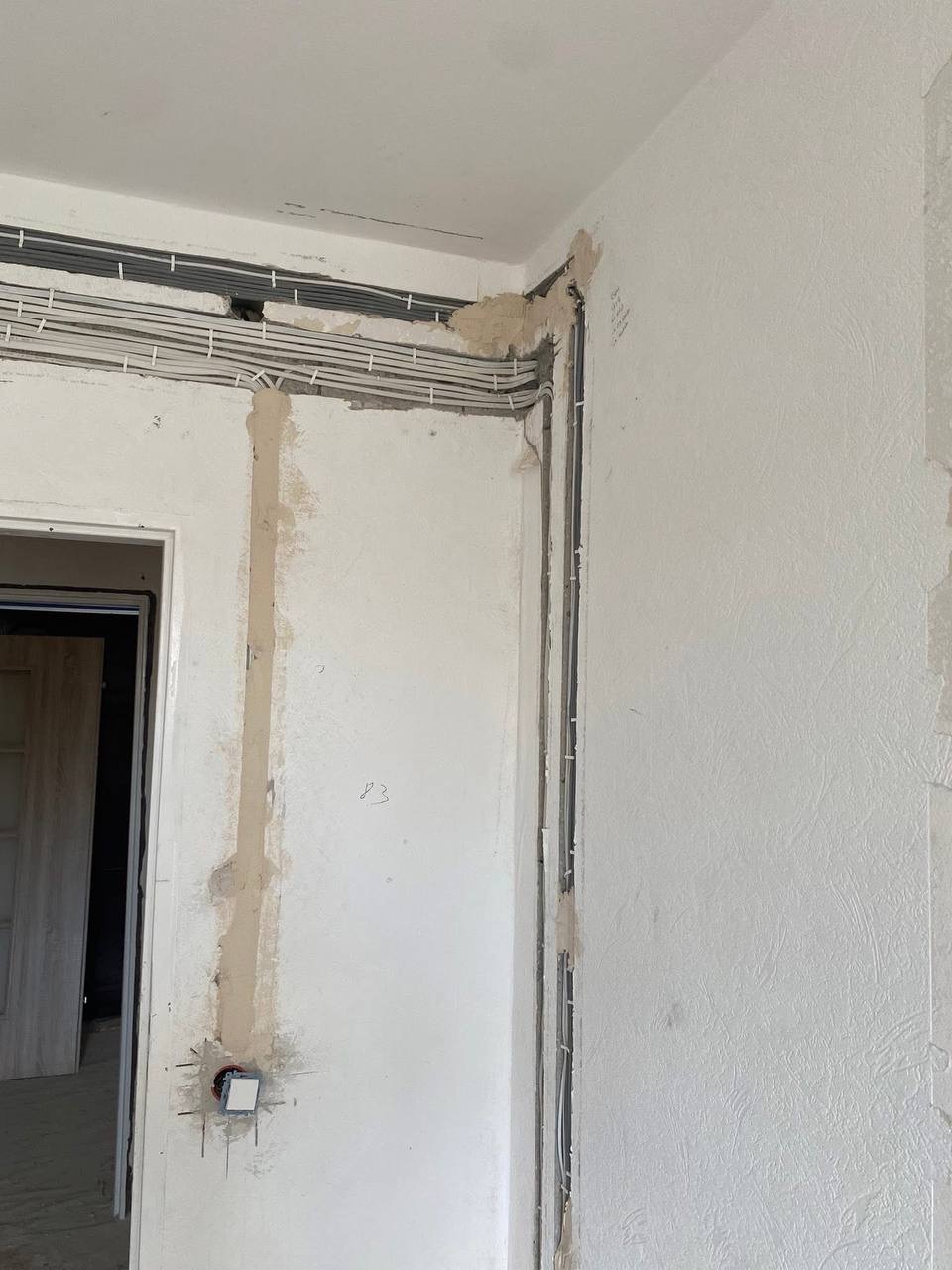 Wnętrze w trakcie prac: kable elektryczne ułożone wzdłuż ściany, przygotowane pod tynkowanie, widoczne puszki instalacyjne i mocowania kabli. Surowy stan wykończenia.