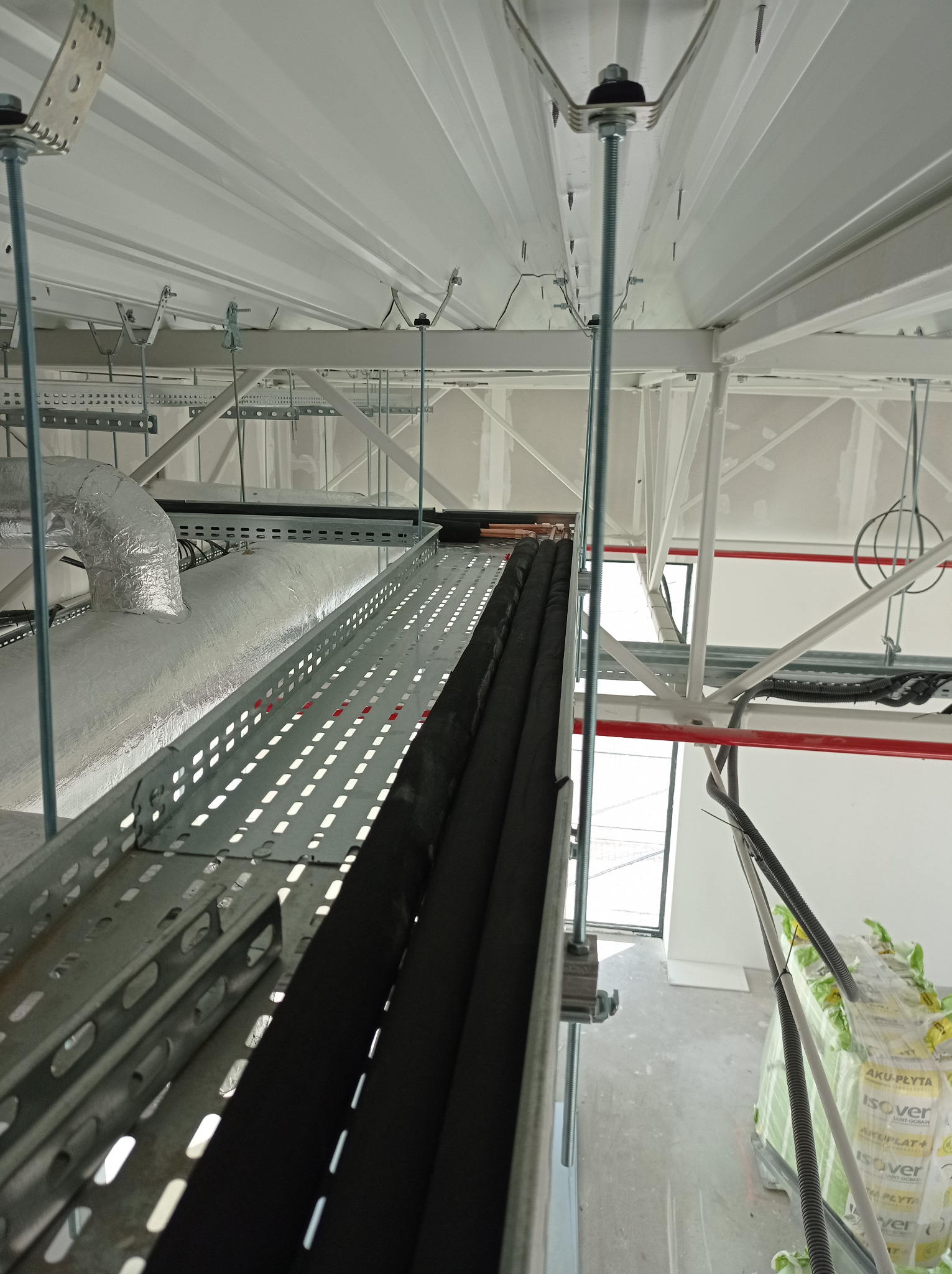 Montaż instalacji klimatyzacyjnej: koryto kablowe z przewodami w izolacji, widoczne elementy mocujące do sufitu, rury wentylacyjne w folii aluminiowej. Ujęcie z dołu.