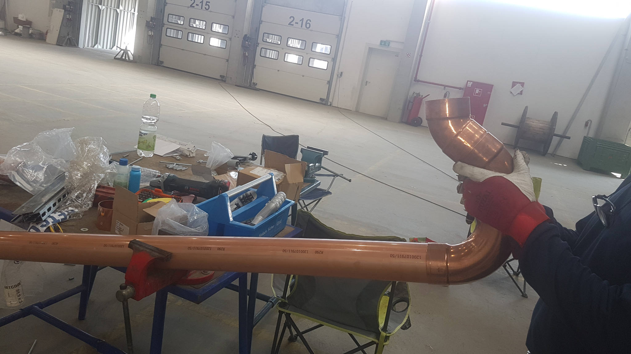 Montaż miedzianej rury klimatyzacyjnej w warsztacie. Rura w imadle, spawanie z użyciem rękawic ochronnych. W tle narzędzia i materiały.