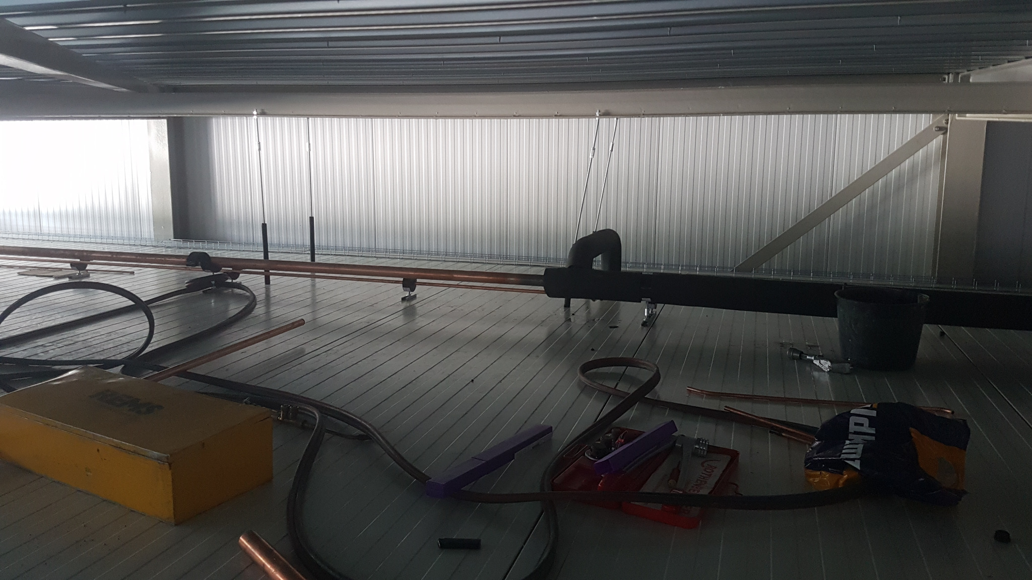 Montaż instalacji klimatyzacji: miedziane rury, narzędzia (REMS, Rothenberger) na metalowej konstrukcji pod sufitem. Widoczne elementy mocujące i izolacja.