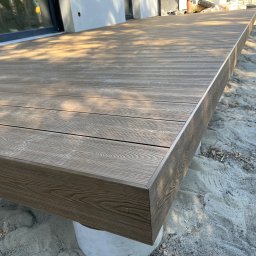 Vk-Bud - Nowoczesny taras z deski kompozytowej w odcieniach brązu, z widoczną strukturą drewna i precyzyjnym wykończeniem krawędzi. Podkonstrukcja na betonowych podporach.