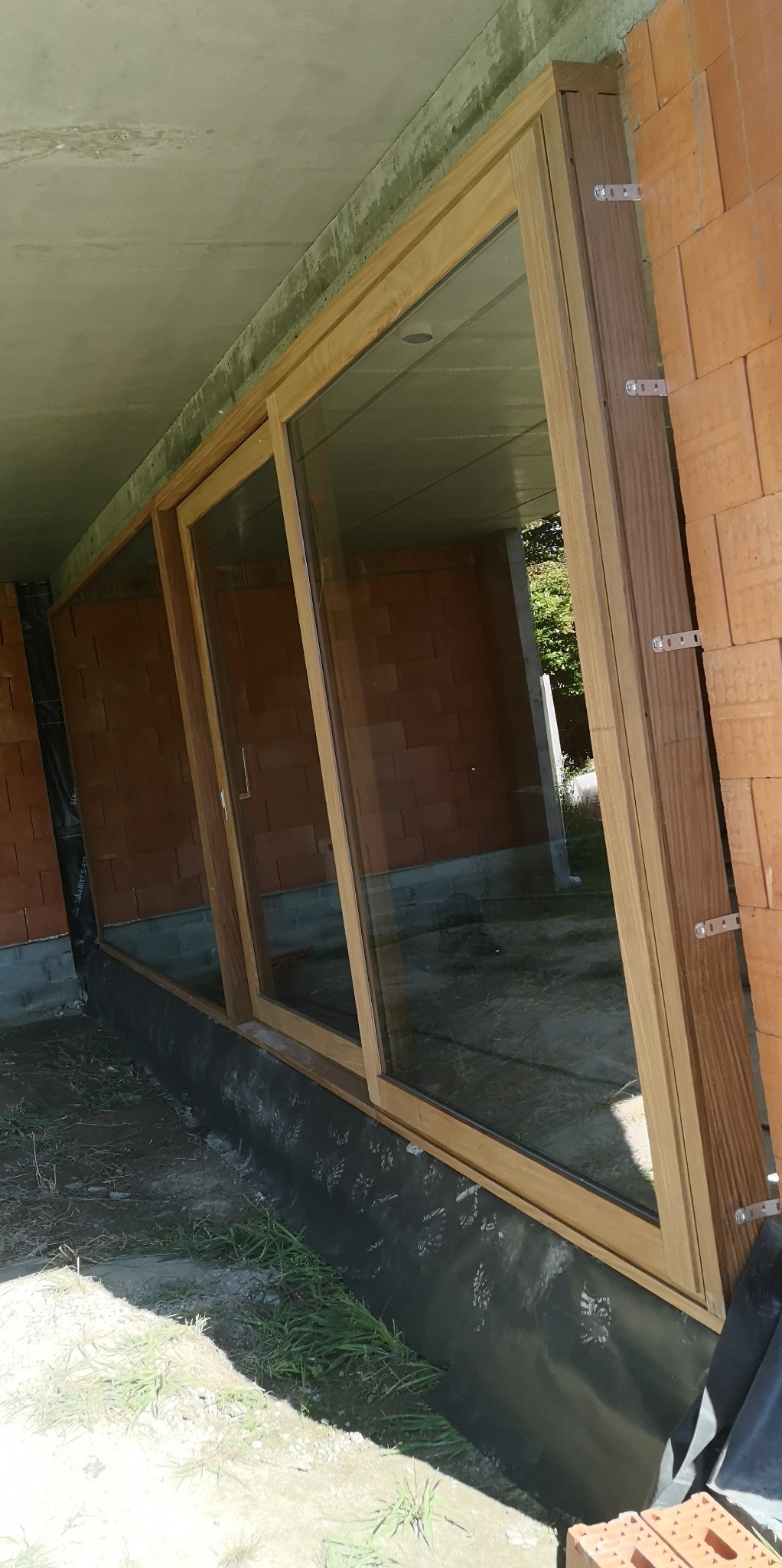 Montaż okien z drewnianą ramą w surowym stanie. Widoczne mocowania do muru z cegieł. Okna zamontowane w otworze, widoczne zabezpieczenie folią.