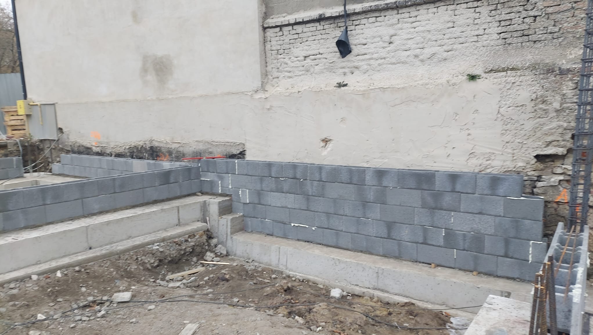 Wznoszenie fundamentów z bloczków betonowych w Katowicach, widoczne zbrojenia i nierówny teren budowy.