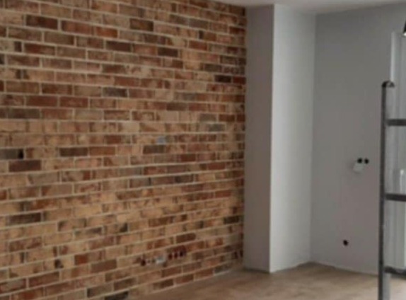 Ściana z cegły dekoracyjnej w surowym wnętrzu, widoczne niedoskonałości spoin i lekkie zabrudzenia, surowy klimat pomieszczenia.