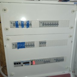 WOJCIECH ANUSZKO EL-WAN - Rozdzielnica elektryczna Eaton z zabezpieczeniami i miernikiem napięcia, widoczne przewody. Część wyłączników zabezpieczona taśmą. Ujęcie z bliska, z góry.