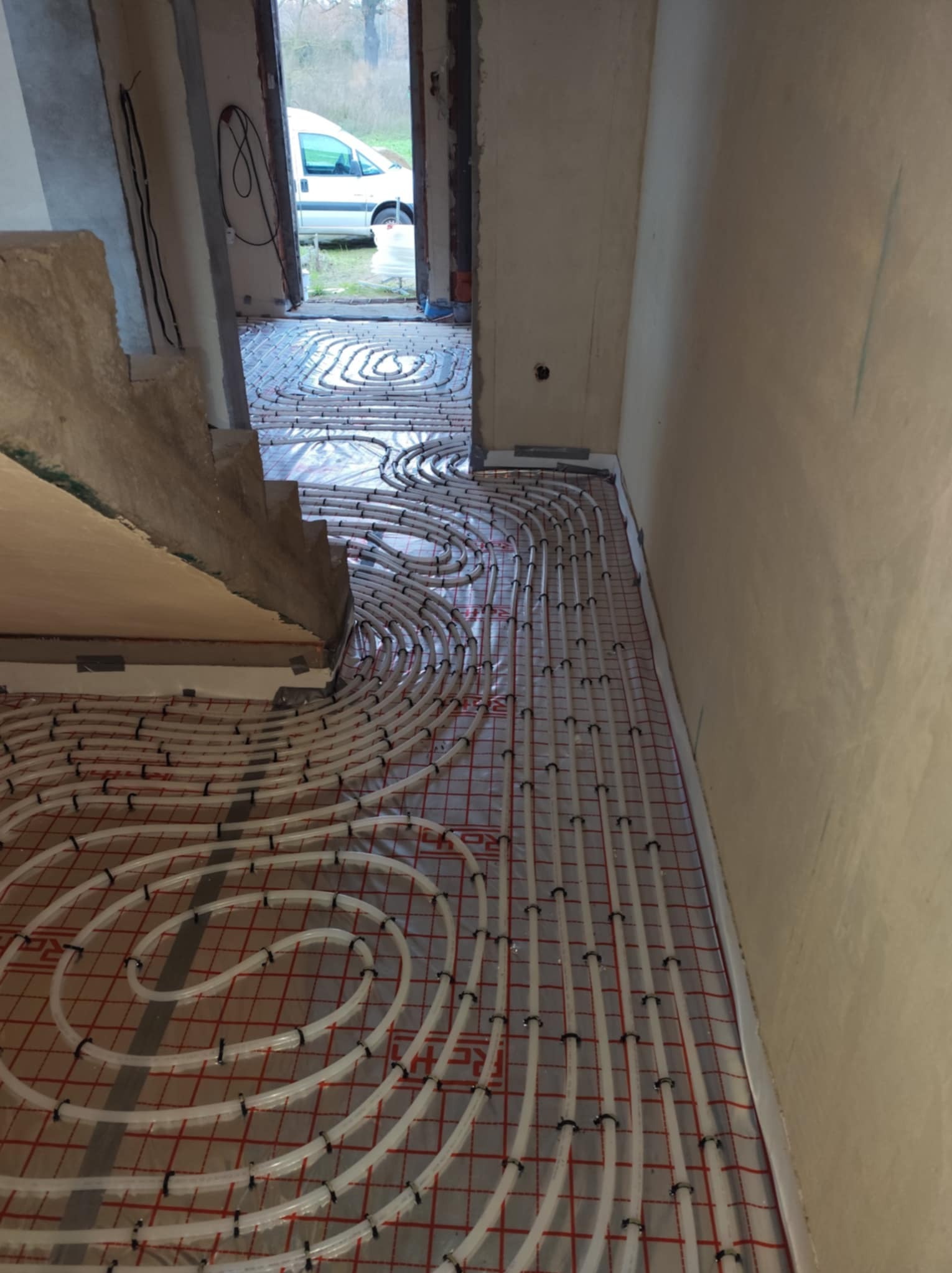 Rozłożone rury ogrzewania podłogowego na folii z siatką, widok z góry na etap instalacji w surowym wnętrzu domu.