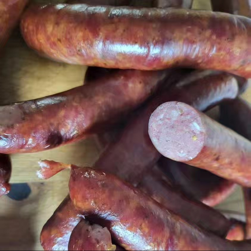 Kiełbasa wiejska wędzona, z widocznym przekrojem ukazującym strukturę mięsa, ułożona na drewnianej desce.