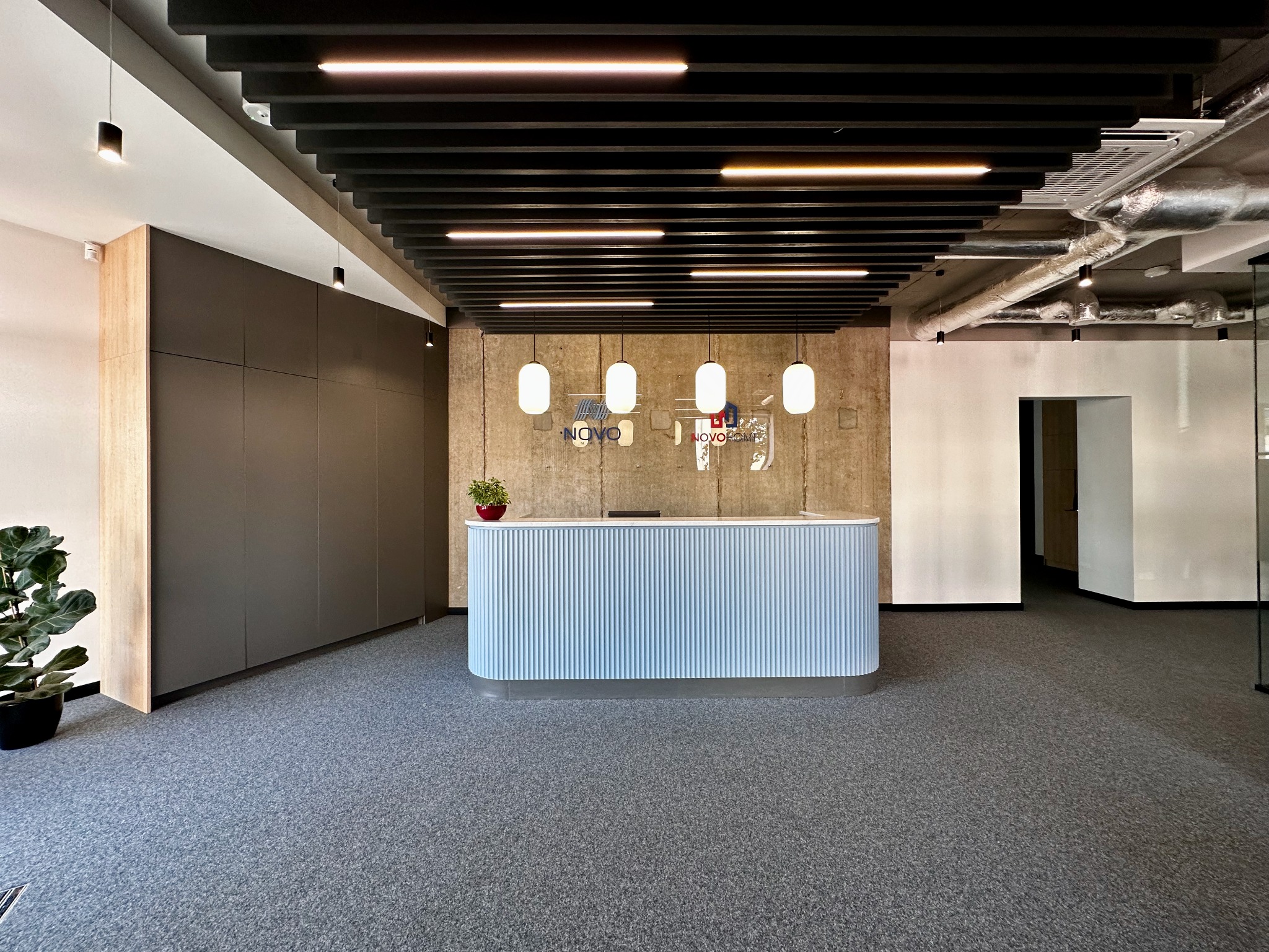 Nowoczesne biuro z recepcją w odcieniach szarości i błękitu, betonowa ściana w tle z logo firmy, sufit z czarnymi belkami i oświetleniem liniowym.