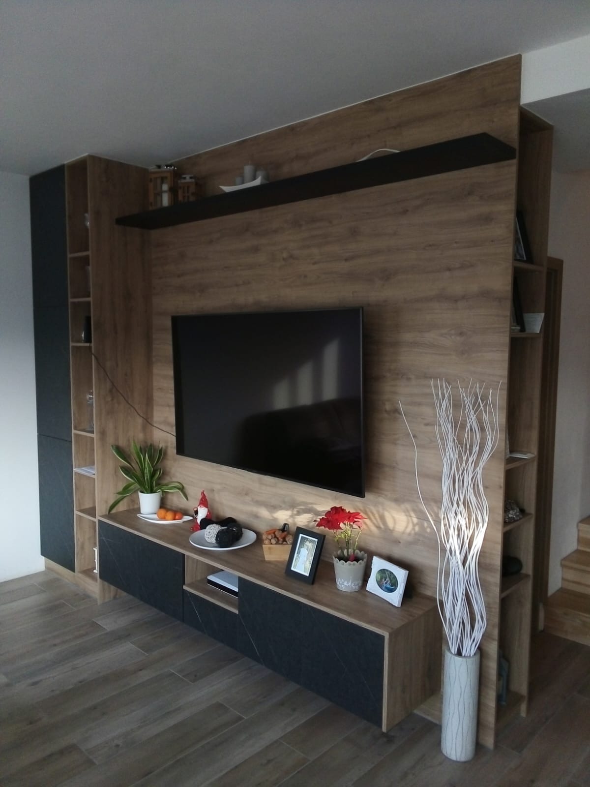 Zabudowa RTV z szafkami w odcieniach drewna i grafitu, półki z dekoracjami, podświetlenie LED, na parkiecie. Projekt nowoczesny z elementami dekoracyjnymi.